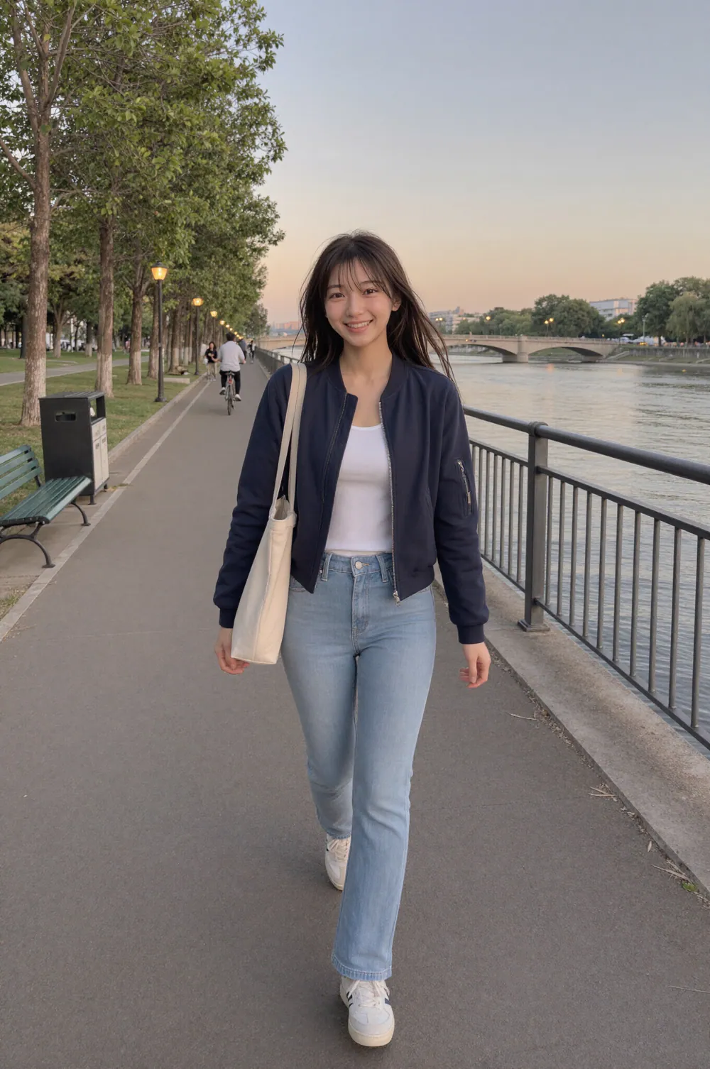 해 질 녘 강변 산책로를 카메라 쪽으로 걸어오며 웃는 Riho. 남색 점퍼에 청바지를 입고 어깨에 에코백을 멨고, 뒤로 다리와 막 켜진 가로등이 보인다